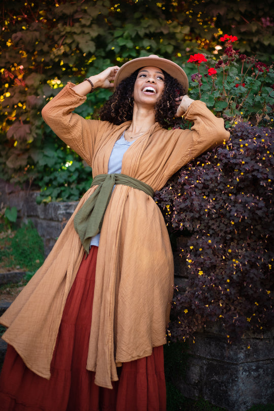 Woman is clothed in gold cloak tied over tank top and maxi skirt.