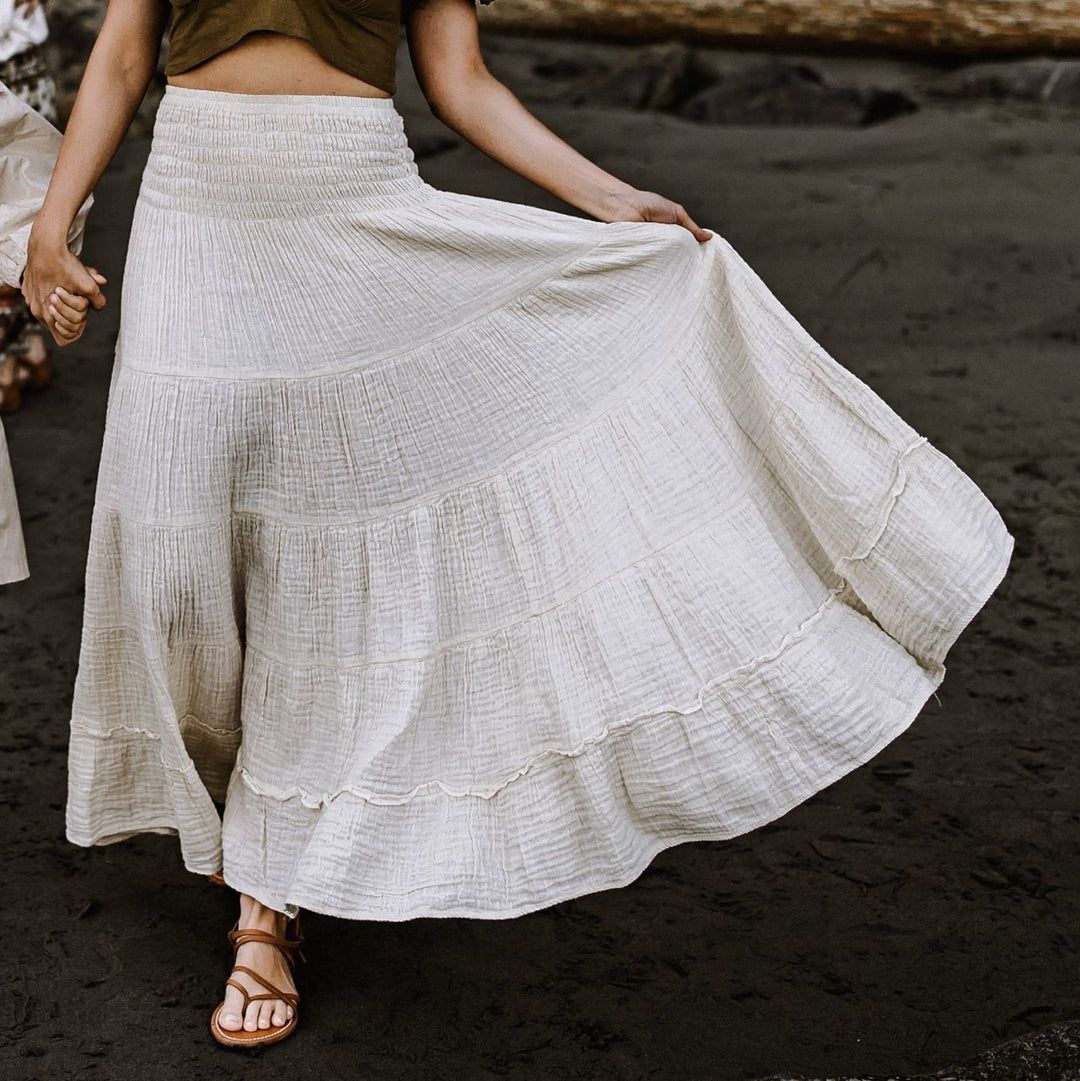 Model wears long tiered maxi skirt with ruffles. The skirt is un-dyed. She holds the hand of a child.
