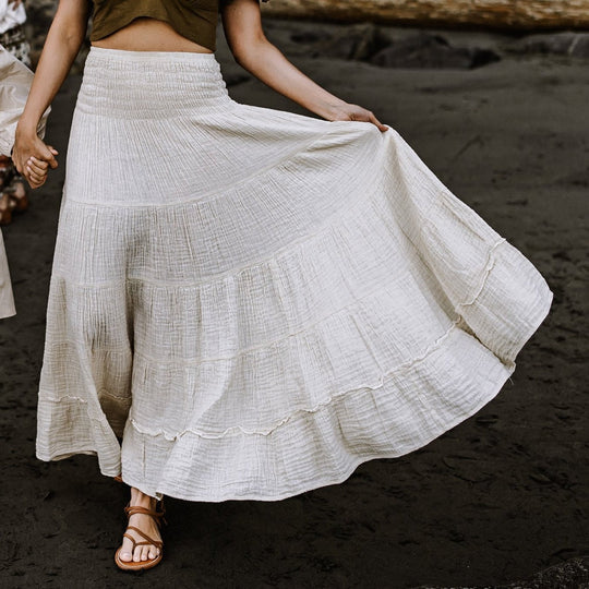 Model wears long tiered maxi skirt with ruffles. The skirt is un-dyed. She holds the hand of a child.