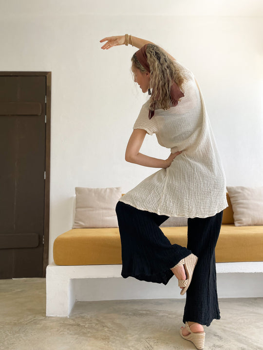 Female in dancer pose wearing un-dyed short dress over long pants.