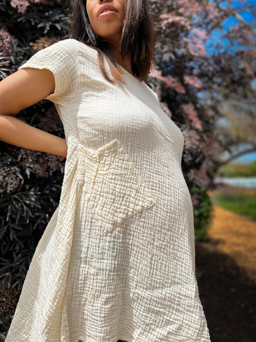 Woman shows off pregnancy in a textured white short-sleeved dress with pockets.