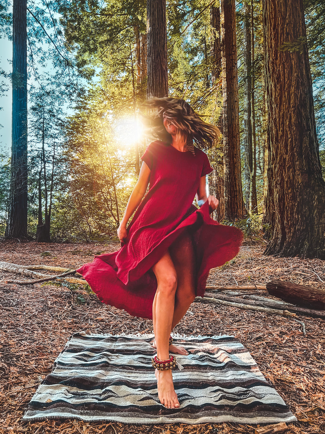 Woman in forest dances on a blanket wearing a flowing red dress.