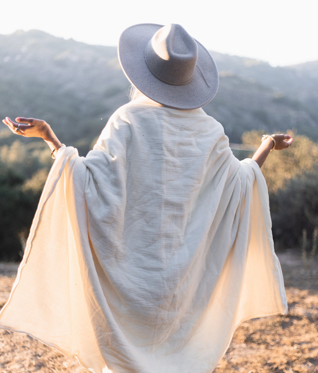 Woman greets the sun wrapped in large white blanket.