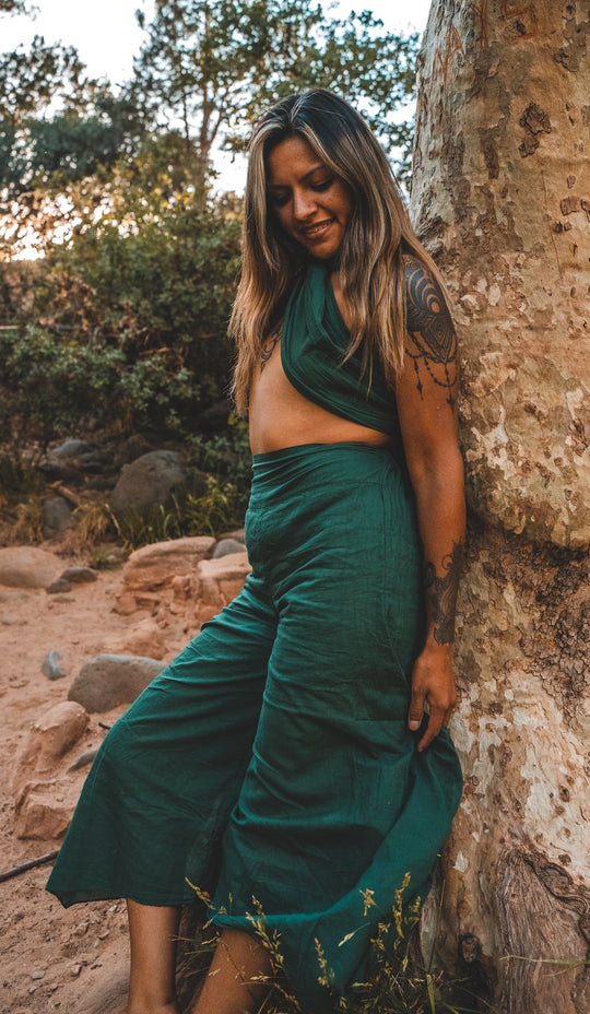 Woman has on emerald green dance pants and matching green wrap top. She stands against a rock.