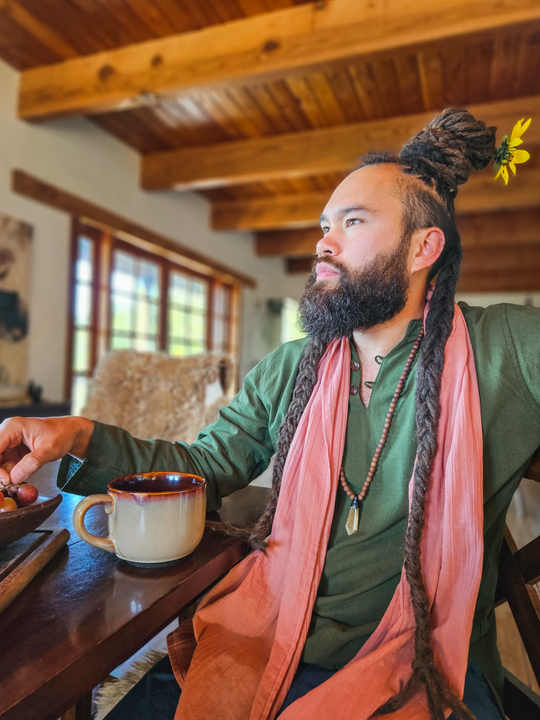 Man sits at kitchen table dressed in long scarf draped around neck and green shirt.