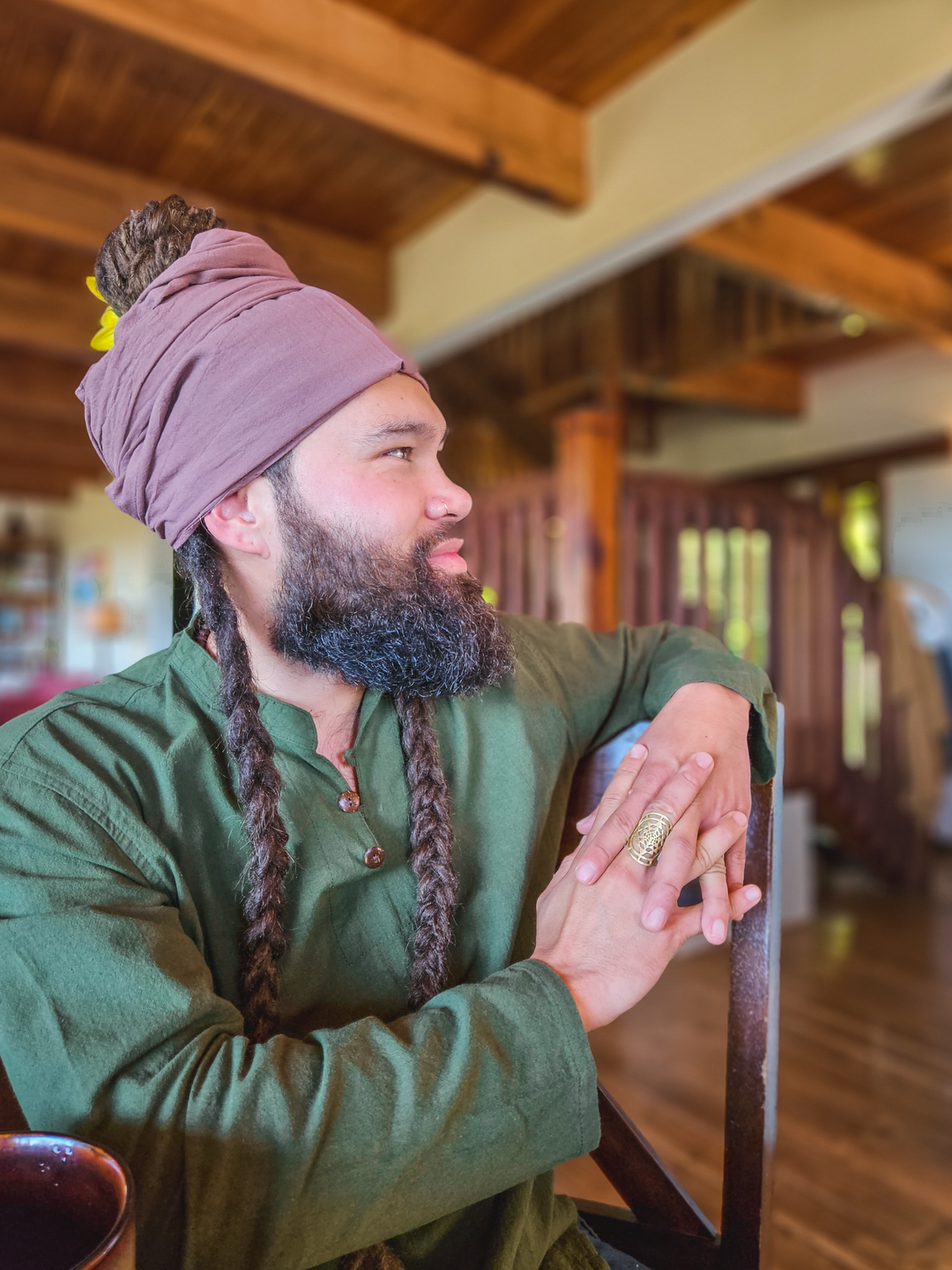 Man has scarf tied as turban on head. He is wearing a green shirt and sitting at kitchen table.