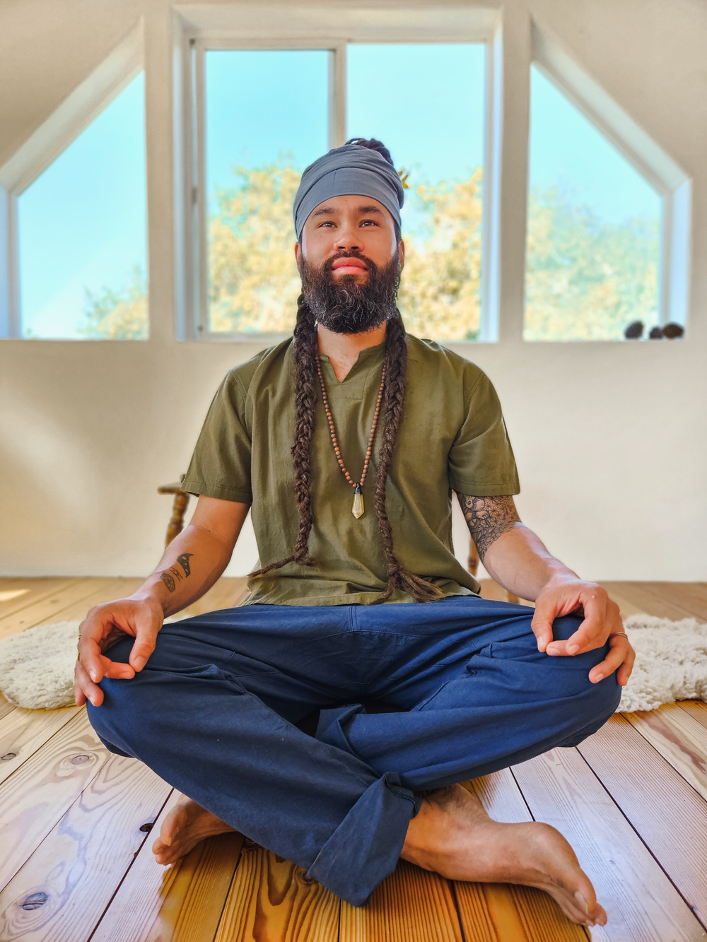 Male model wears long scarf as a head cover. He sits in meditation pose wearing green shirt and blue jogger pants.
