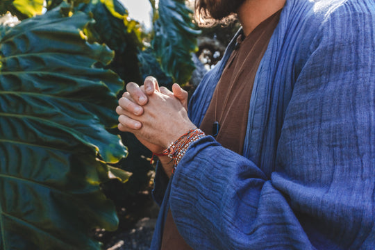 Model dressed in bright blue fabric over a brown shirt  clasps his hands in front of chest.
