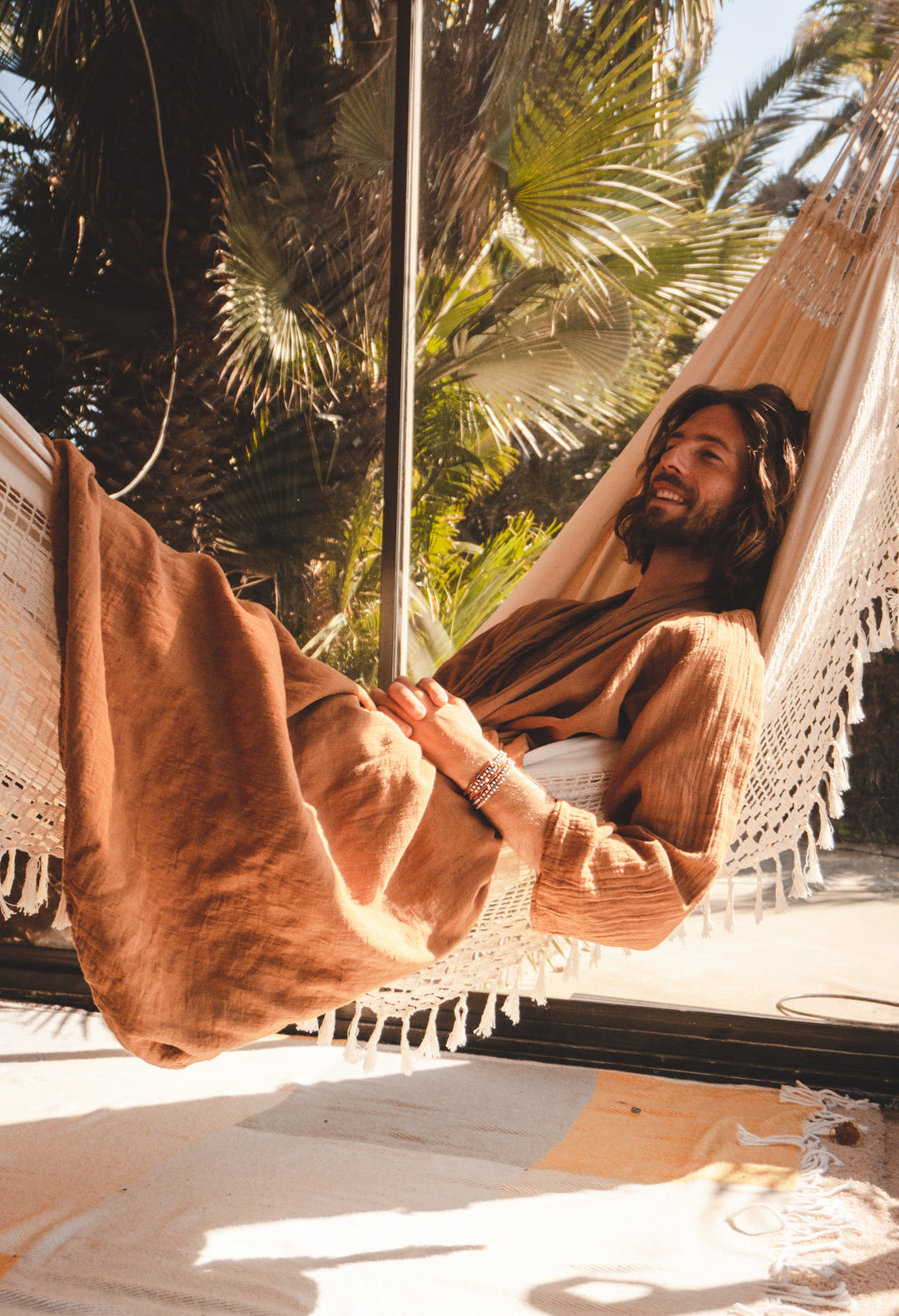 Man lounges in brown robe while relaxing in hammock.