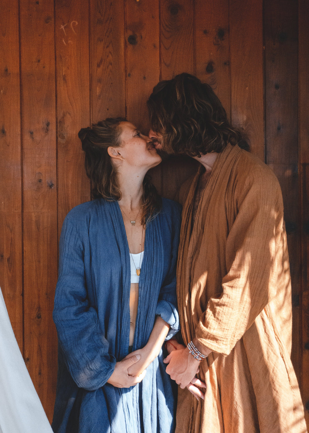 Man and woman hold hands and kiss, each wearing a cloak.