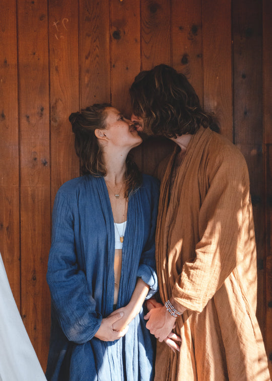 Man and woman hold hands and kiss, each wearing a cloak.