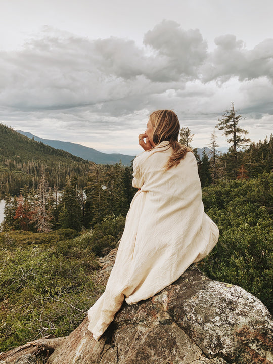 Woman sits on rock wearing large white wrap.