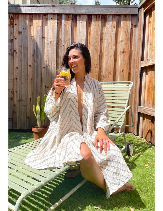 Model sits outside on lawn chair draped in pinstripe cloak and enjoying yellow beverage.