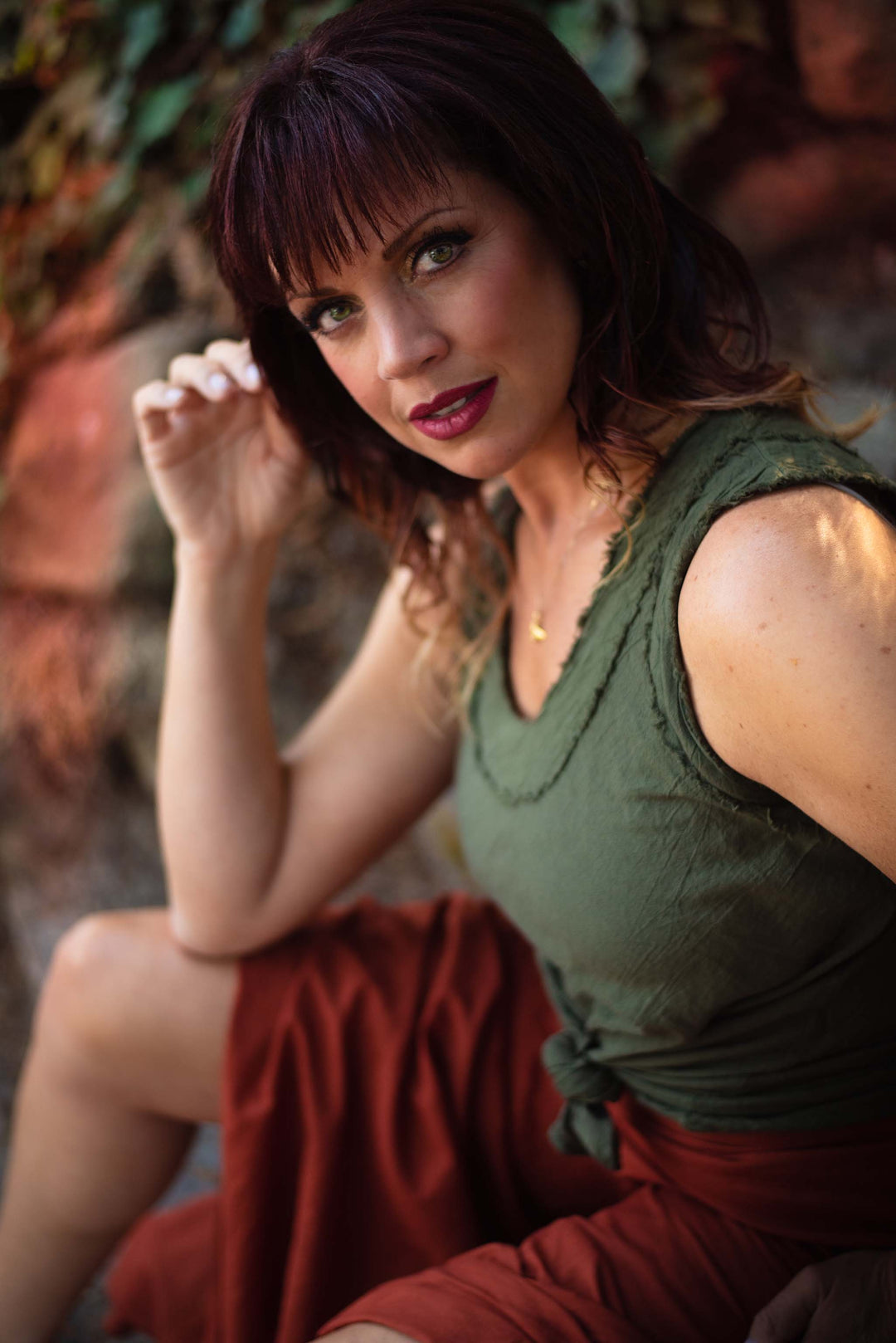Female model is wearing olive green tank top and rust-color skirt.
