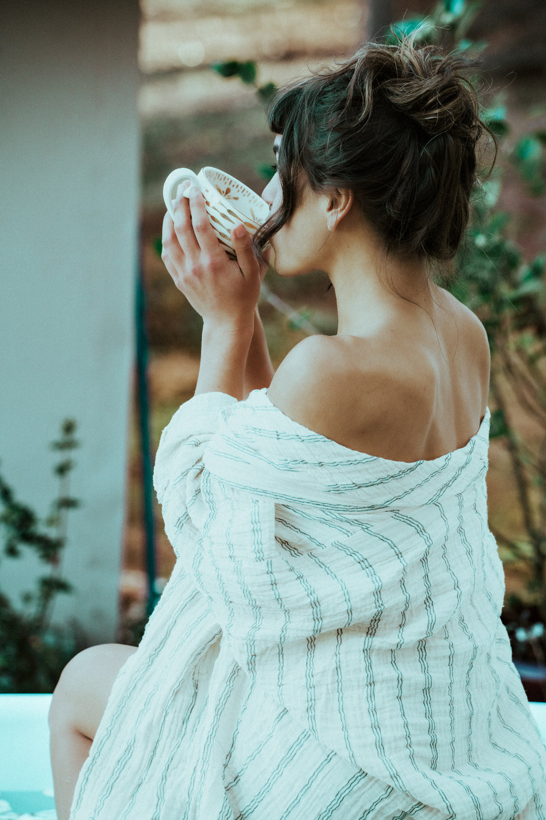 Back of woman wearing striped robe that is loosely wrapped and falling off shoulders.