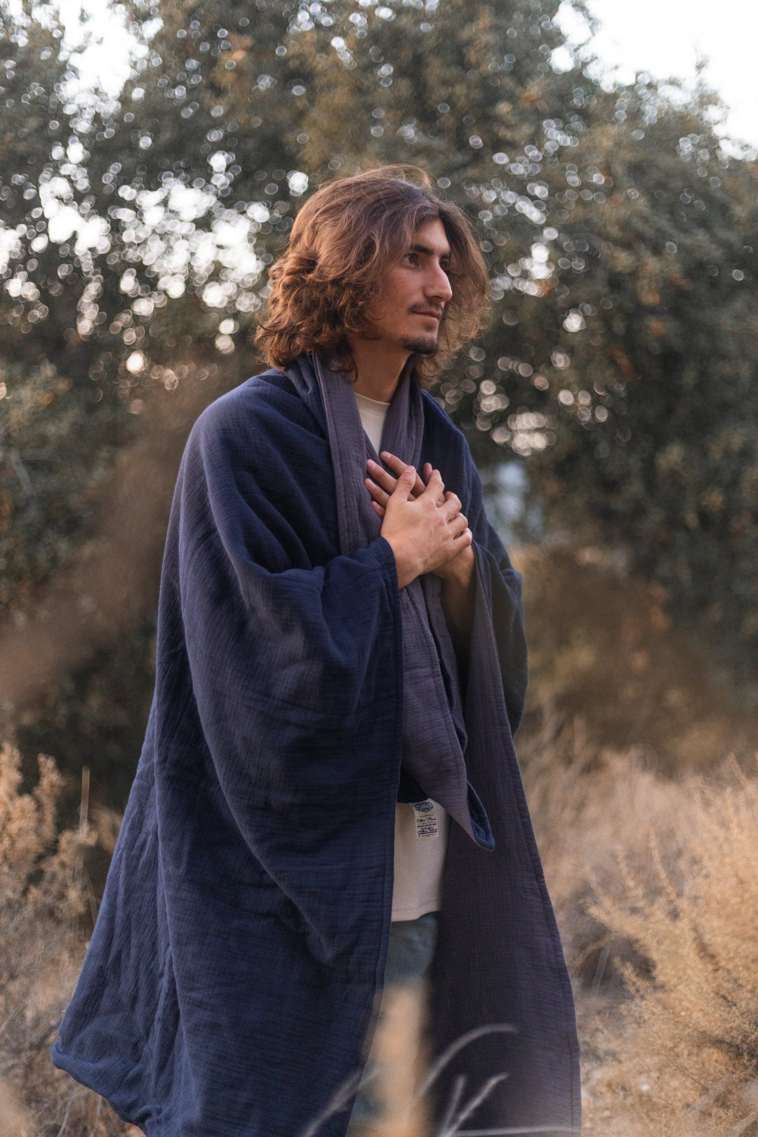 Man has hands at heart wrapped in a large blue blanket.