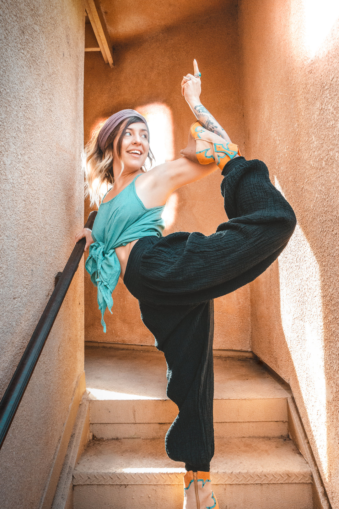Model holds arabesque pose dressed in long yoga pants, tank top and head scarf.