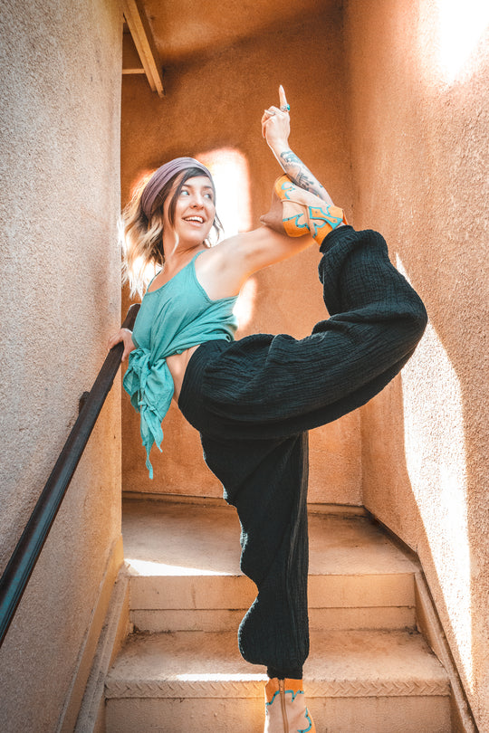 Model holds arabesque pose dressed in long yoga pants, tank top and head scarf.