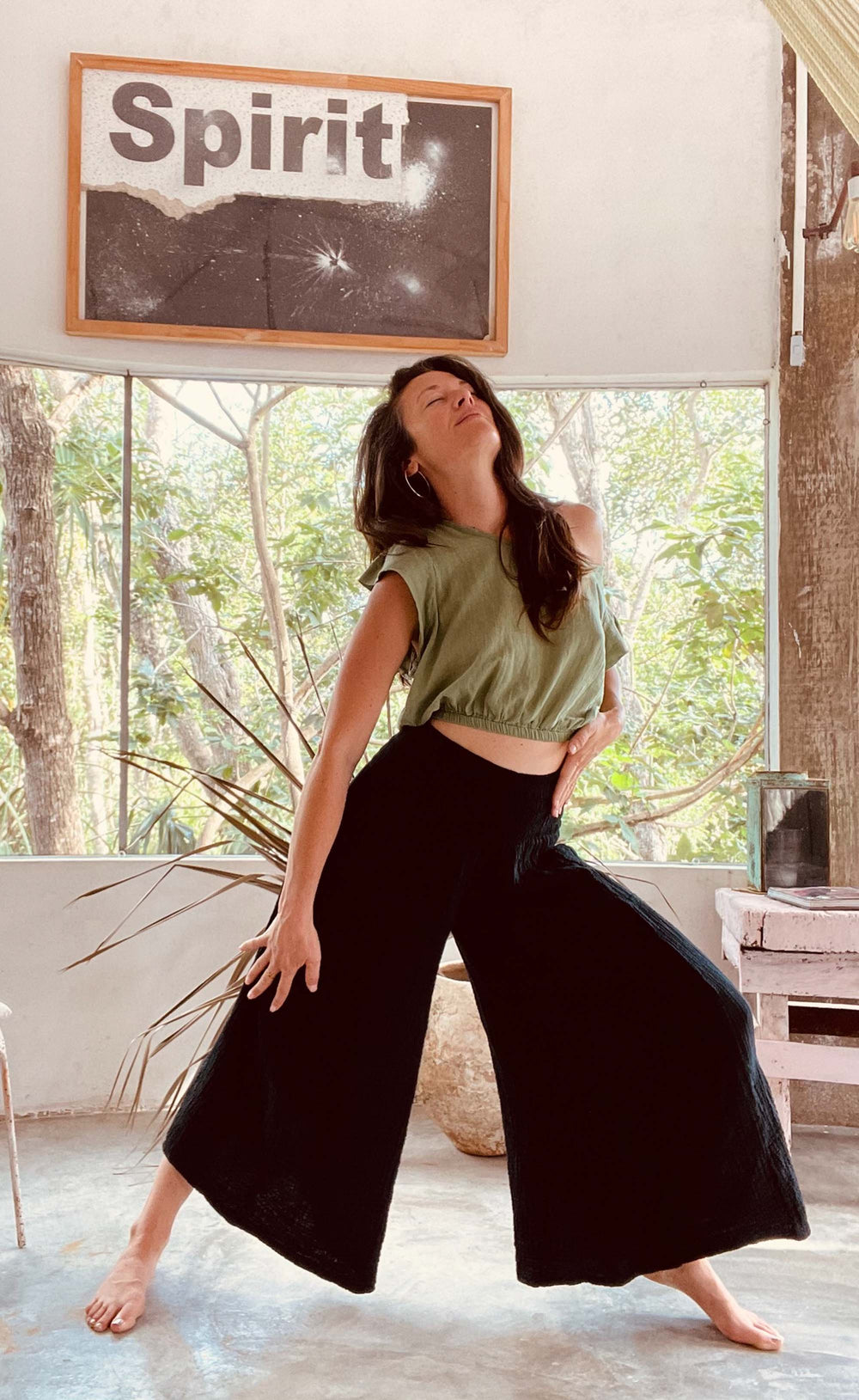 Woman poses in wide-legged stance wearing off-the-shoulder green crop top and black pants.