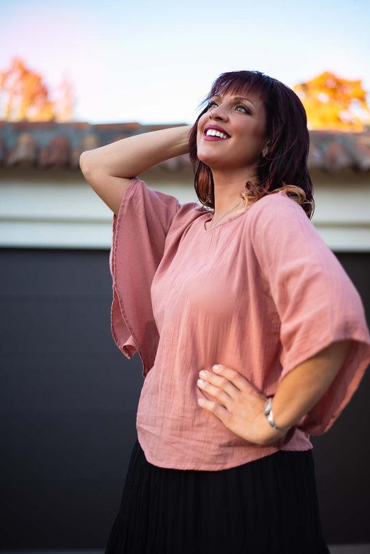 Female has on a pink petal top with wide sleeves and black skirt.