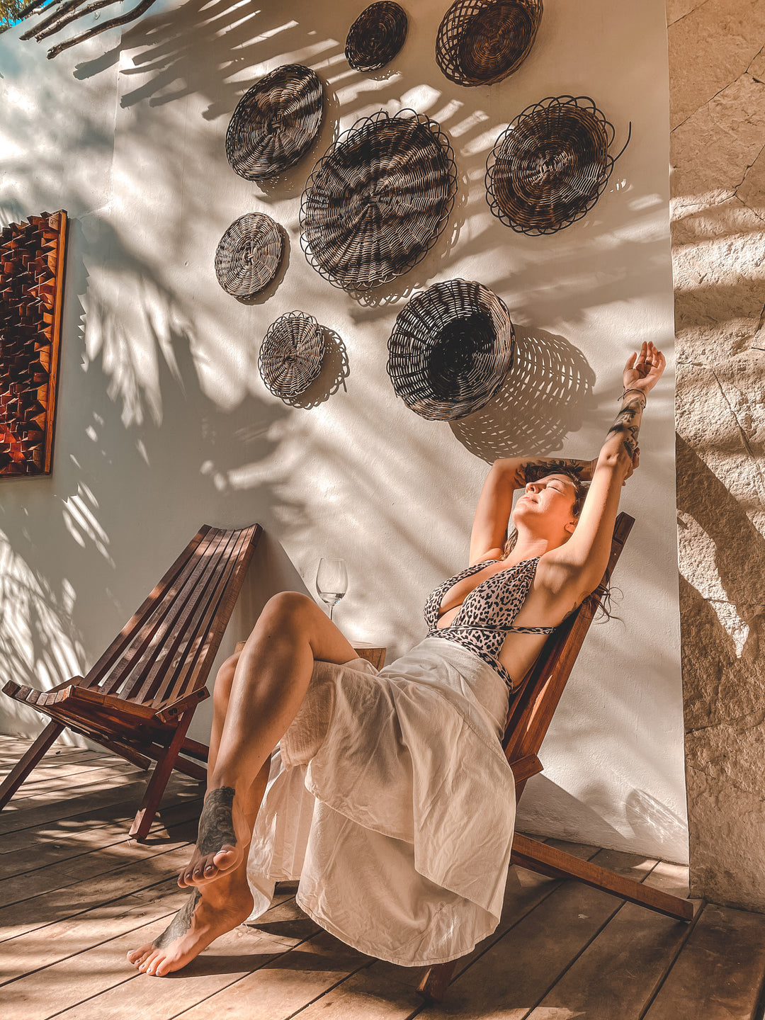 Woman relaxes back in wooden chair wearing skirt over bathing suit.