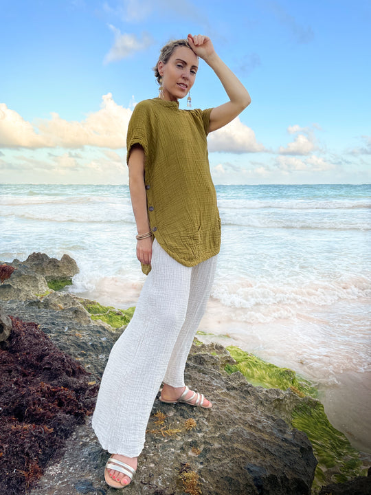 Woman has on short-sleeved top and white lounge pants. She stands on a rock by water.