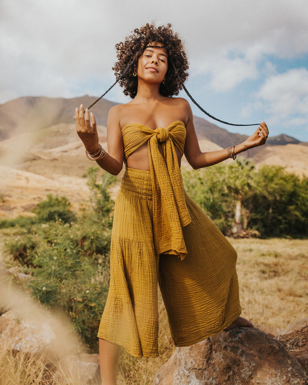 Female clothing model wears gold wrap tied as a bikini top paired with loose gold pants. 