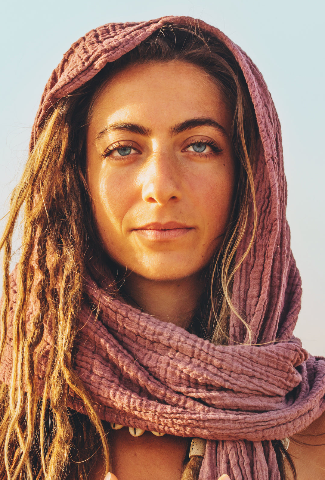 Model poses with earthen rose color gauze scarf around her head and neck.