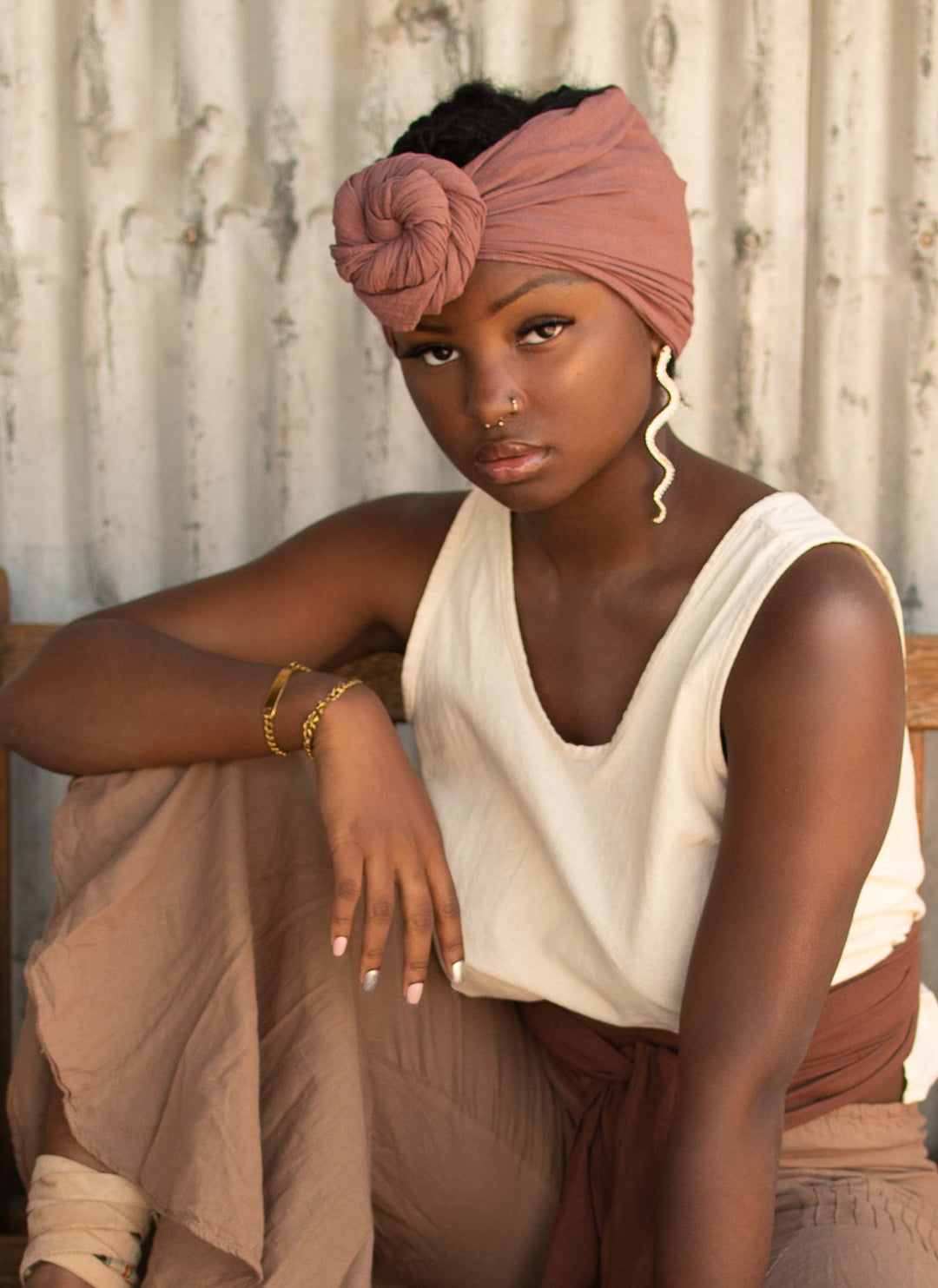 Model has head wrap tied and knotted around her hair. She's wearing an un-dyed tank top, brown belt and brown lounge pants.