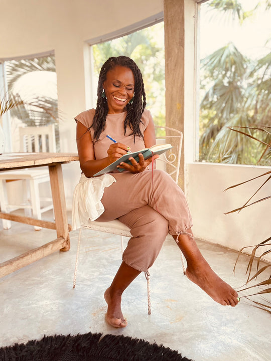 Woman sits in chair writing in notebook. She has on a a pink top and pink leggings.