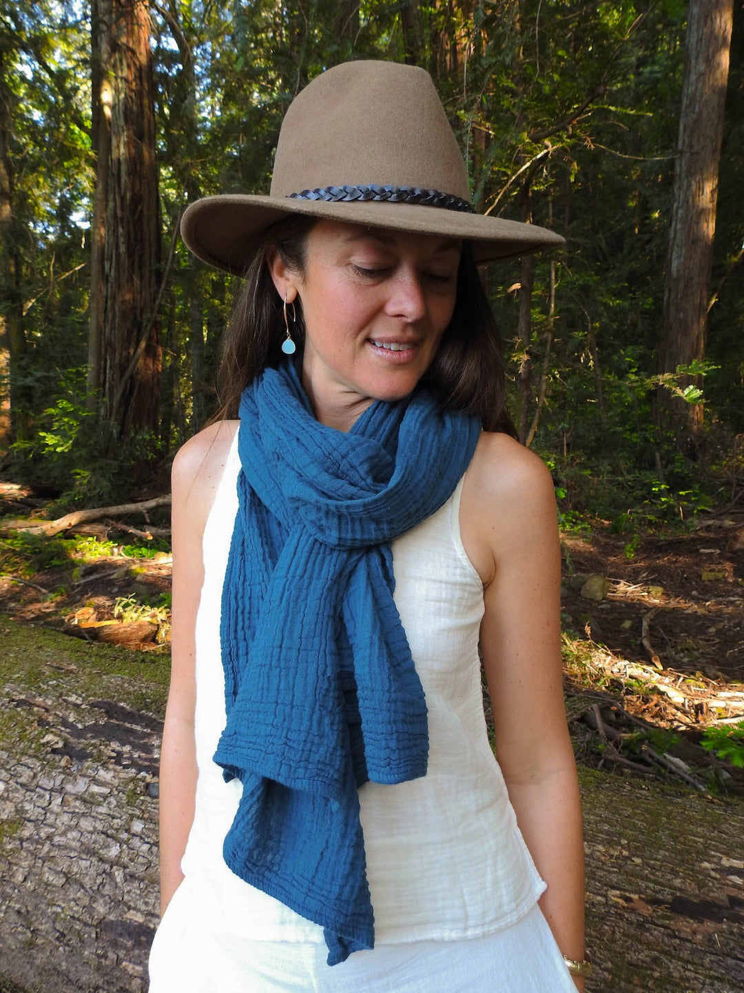 Female model has a blue scarf tied around neck of her white tank top.