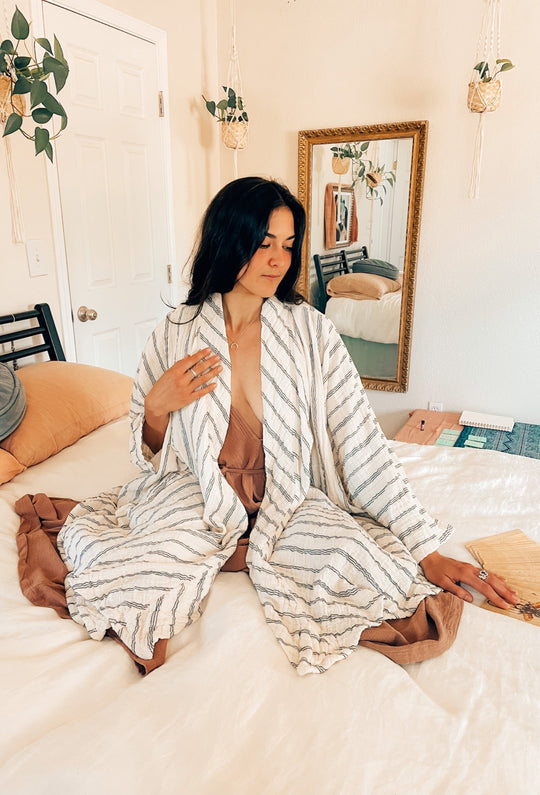 Model sits on bed in cozy striped robe over pajamas.