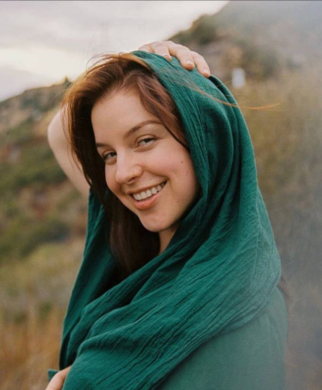 Woman is smiling with head and shoulders covered with long green gauze head scarf.