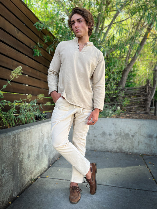 Man stands with one leg crossed over the other. He has on matching un-dyed long-sleeve shirt and pants.