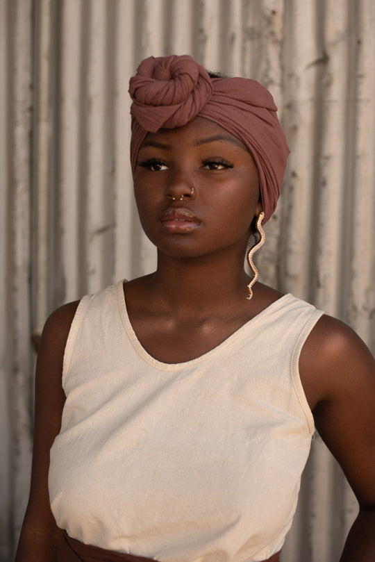 Female model with nose rings and long snake-like earrings wears head wrap tied in front and a natural white tank crop top.