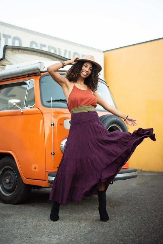 Model has orange cami tucked into purple maxi skirt with green belt.