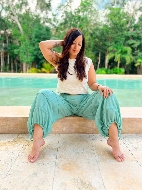 Woman sits at edge of pool wearing white top and aqua balloon pant.