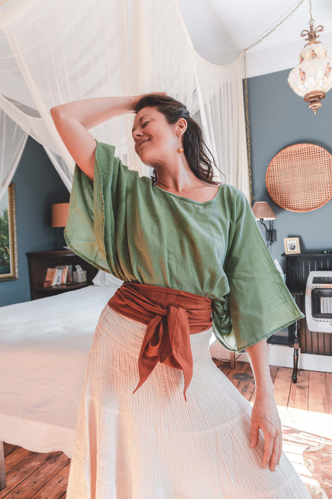 Model wears green flow top with full sleeves, white gauze skirt and orange fabric belt.