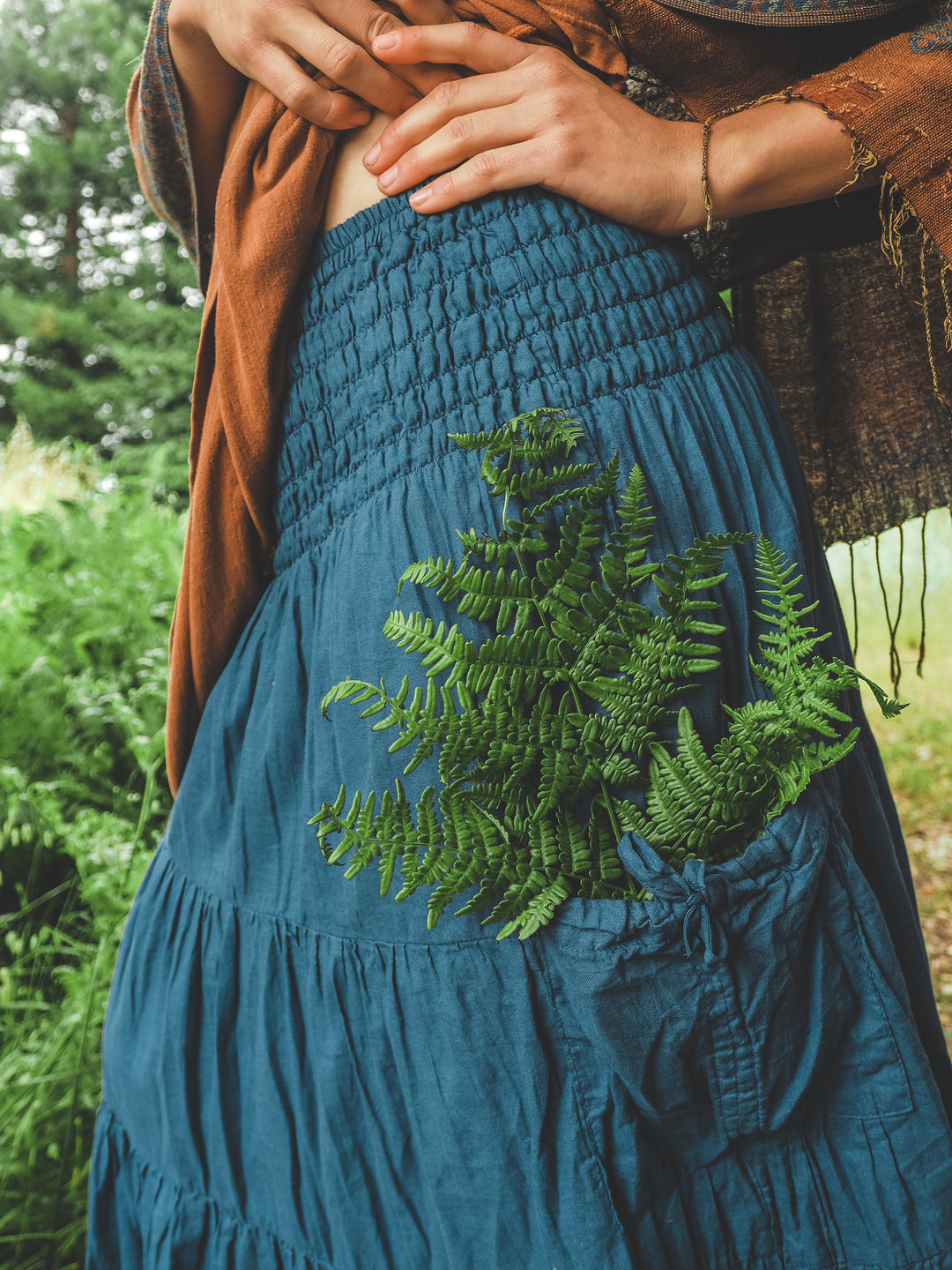 Long blue skirt made from crinkle cotton with large pocket holding greenery.