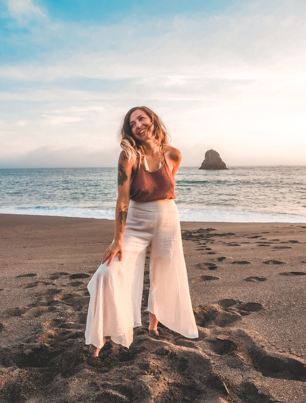 Woman on beach dons lightweight white pants and red tank top.