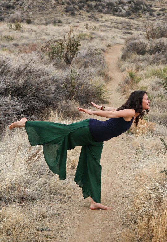 Woman in yoga pose is dressed in navy top and long flowing green pants.