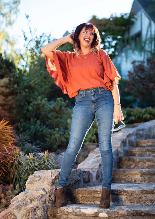 Woman wears shirt with ruffle, flutter sleeves paired with jeans and brown boots.