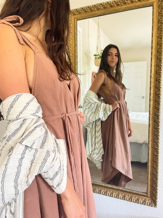 Model wears striped cardigan over long pink dress. She is looking in a mirror.