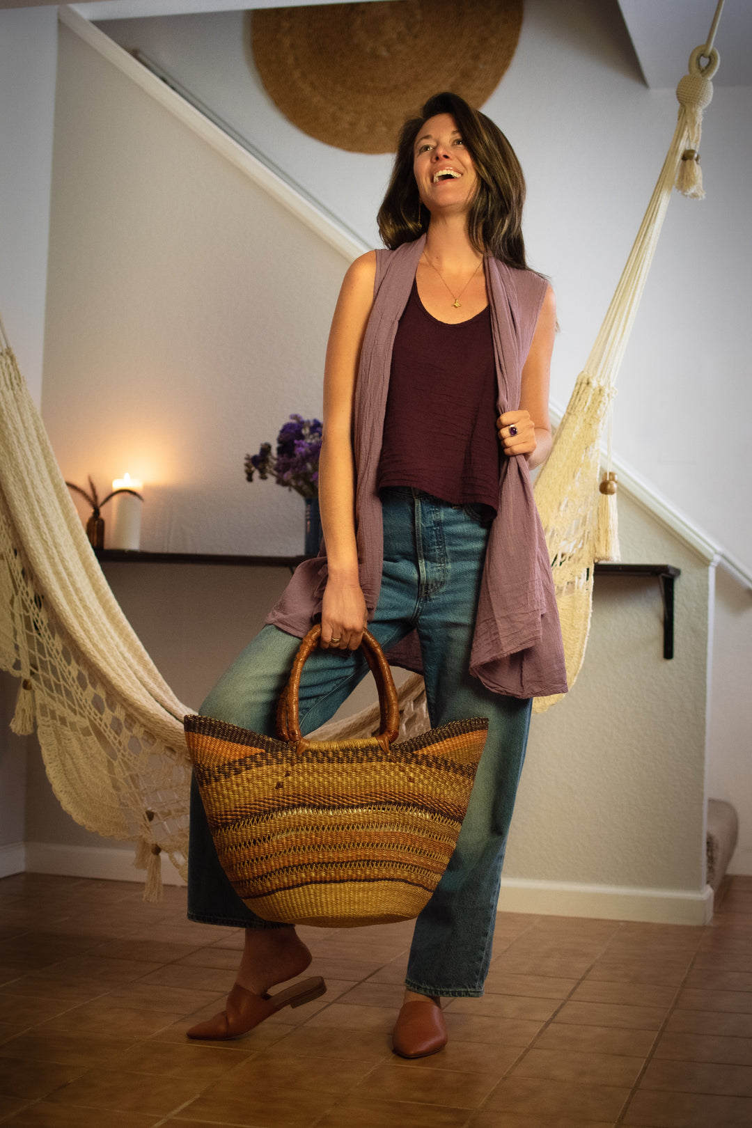 Woman dressed in long purple vest, maroon tank top and jeans. She carries a purse.