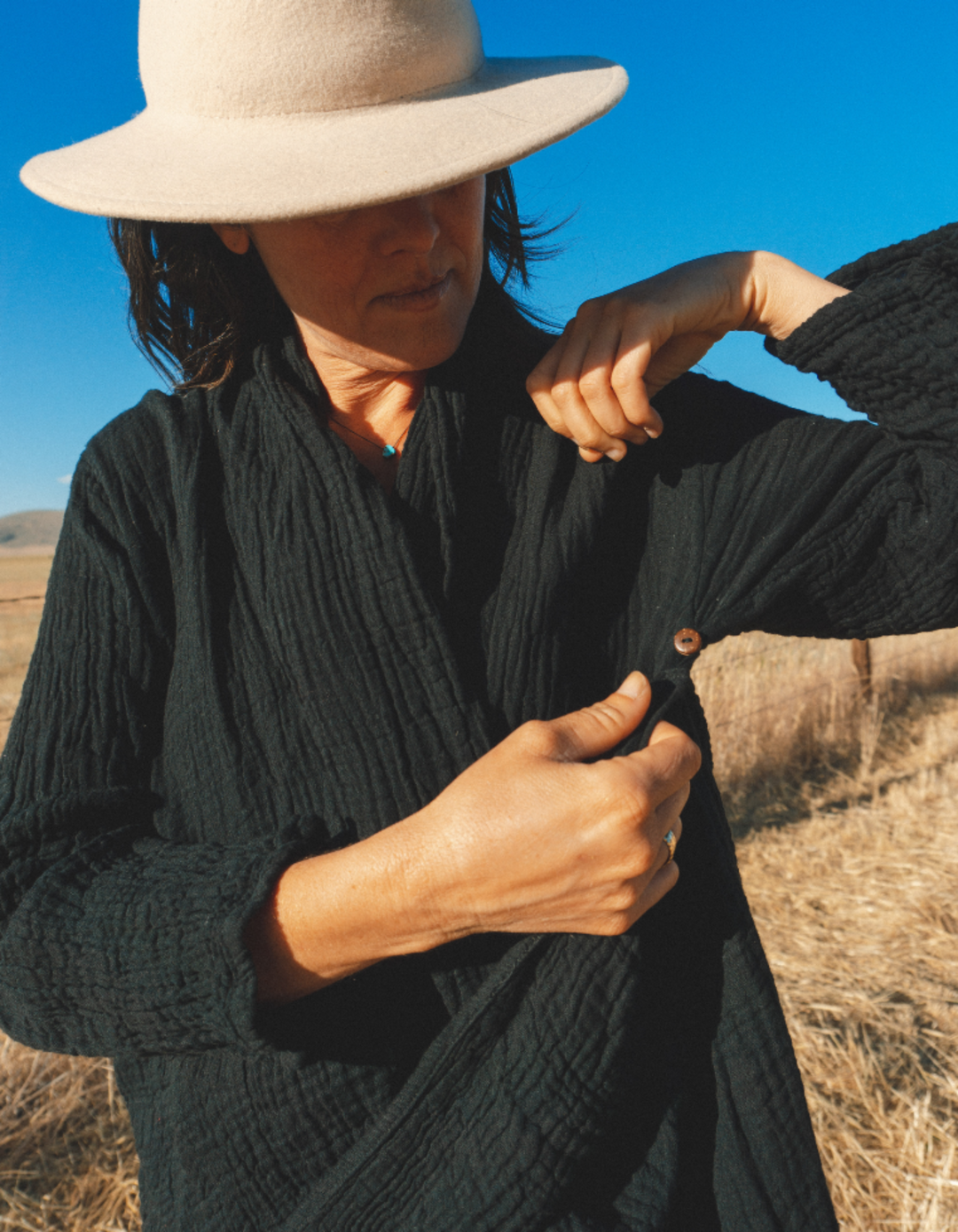 Woman wearing black gauze sweater shows button.