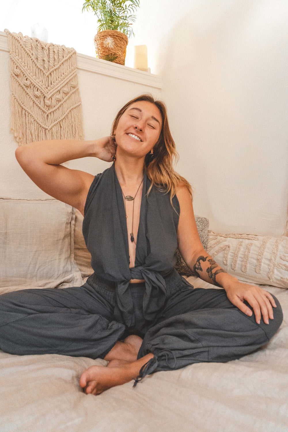 Woman sits with eyes closed in gray two piece wide legged yoga clothing.