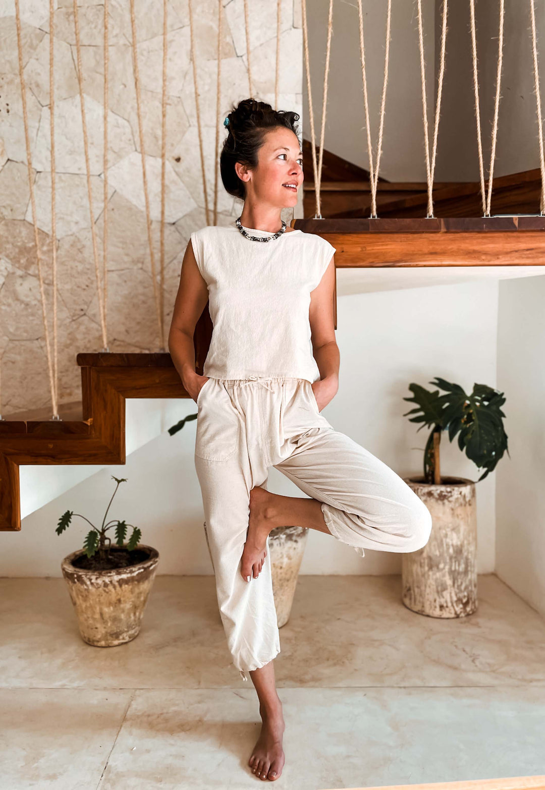 Model stands in tree pose wearing natural white tank top and yoga pants.