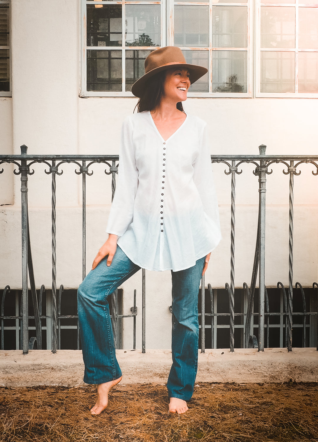 Model is posed wearing long-sleeve, white button down shirt with jeans.