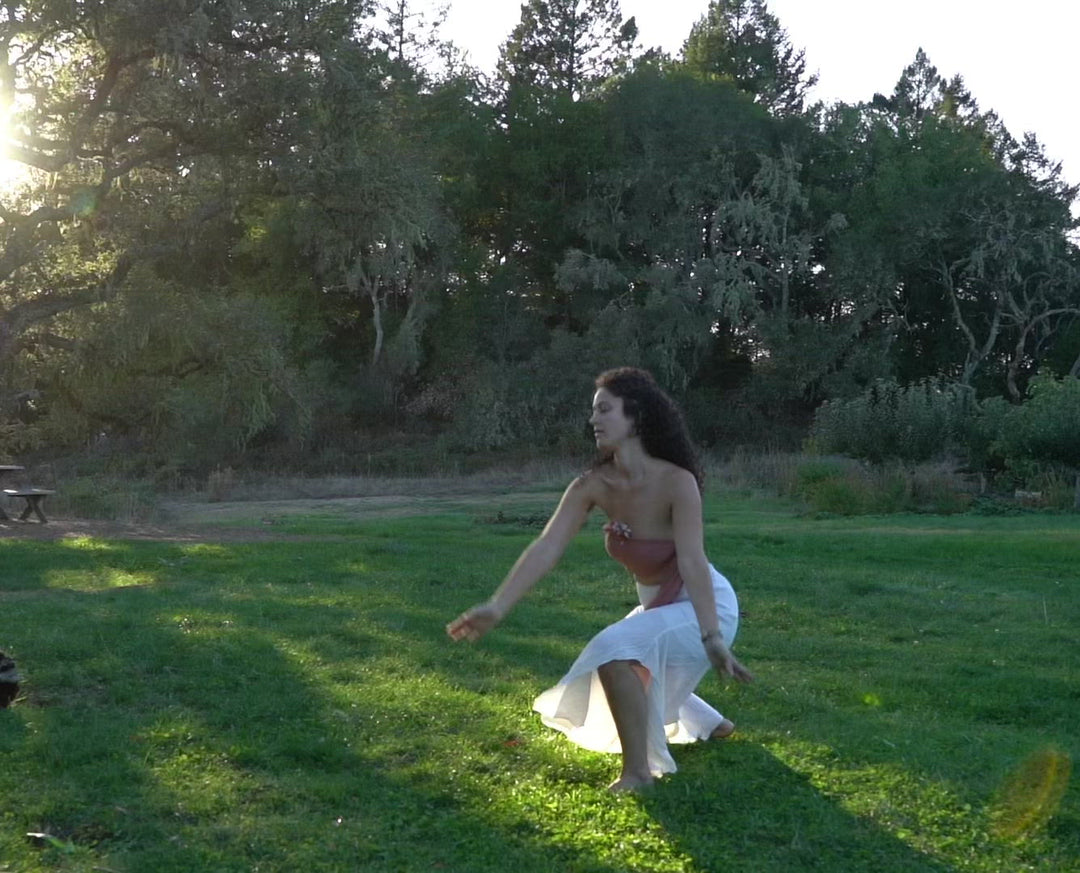 Woman dances in stretchy white pants and pink wrap top.