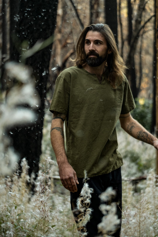 Male in olive green t-shirt and black pants walking through forest.